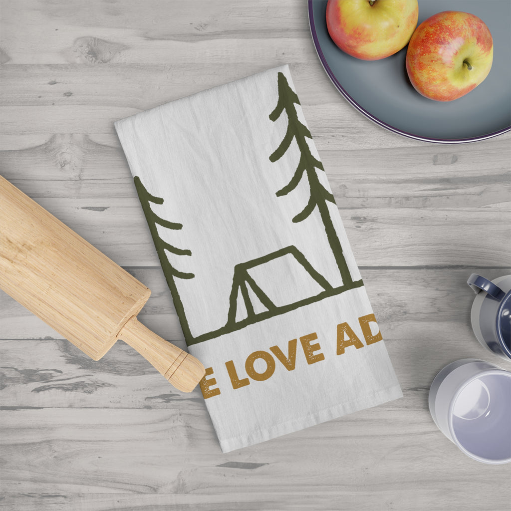 Kitchen towel with nature-themed design and 'We Love ADV' text on a wooden surface with apples and a rolling pin.